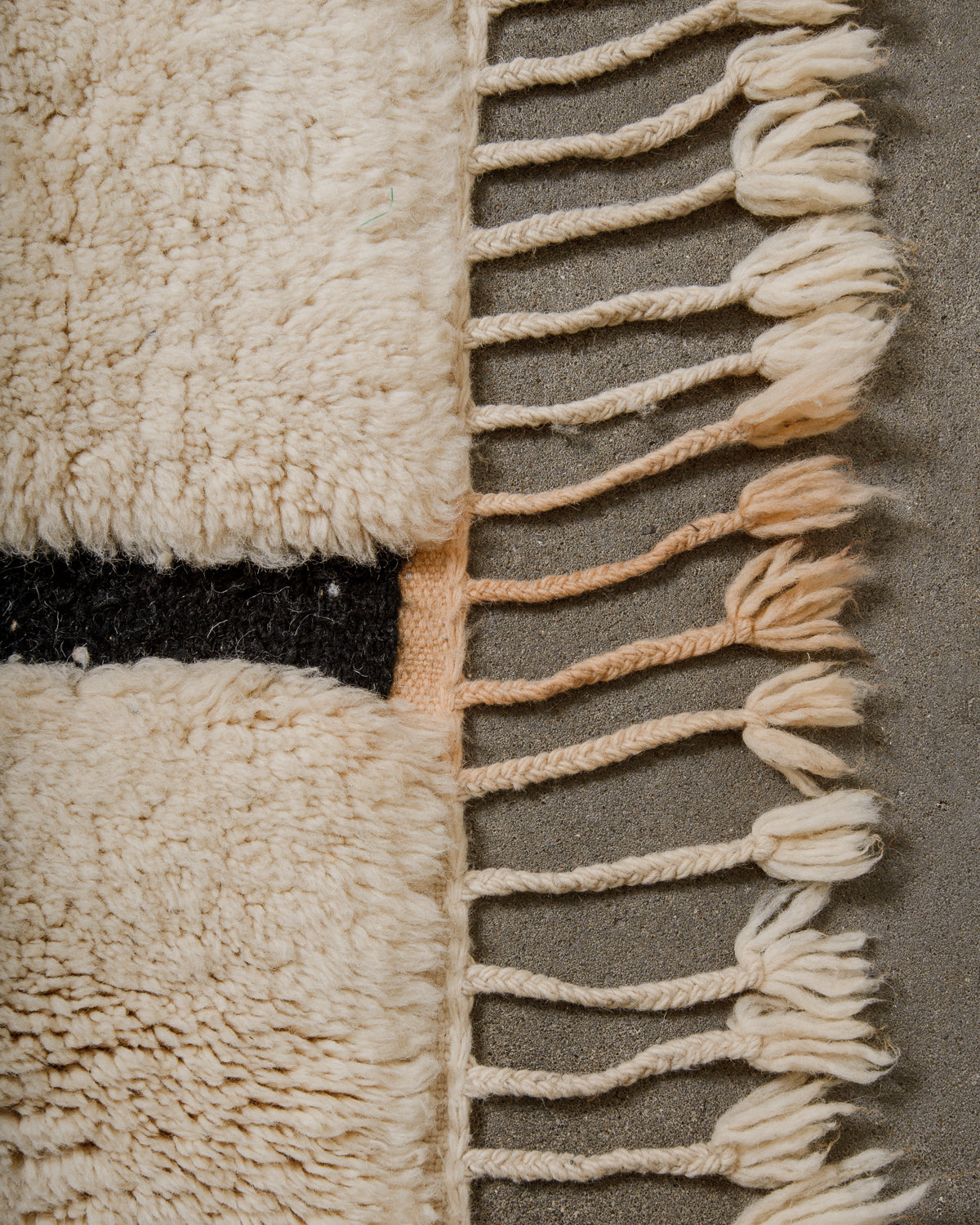 Close-up of a wool rug with tassels and a black design that has discoloured part of the tassels.